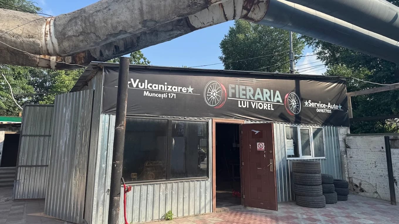 Atelierul de pe Șoseaua Muncești 171: clădirea din tablă cu bannerul FIERĂRIA LUI VIOREL, Vulcanizare și Service-Auto, sub conductele de termoficare.